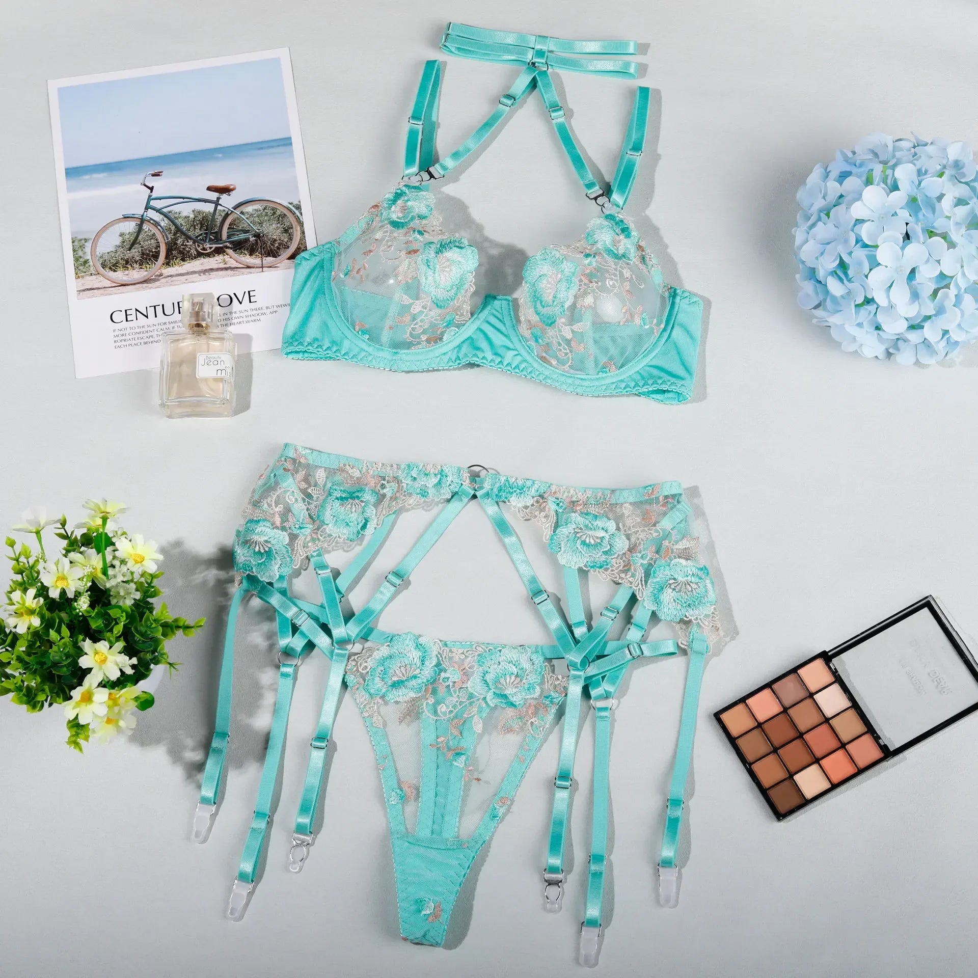 Teal lingerie set with floral design on a light gray surface with flowers and a magazine.
