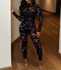 Woman wearing a black lace jumpsuit standing in a room with wooden flooring.