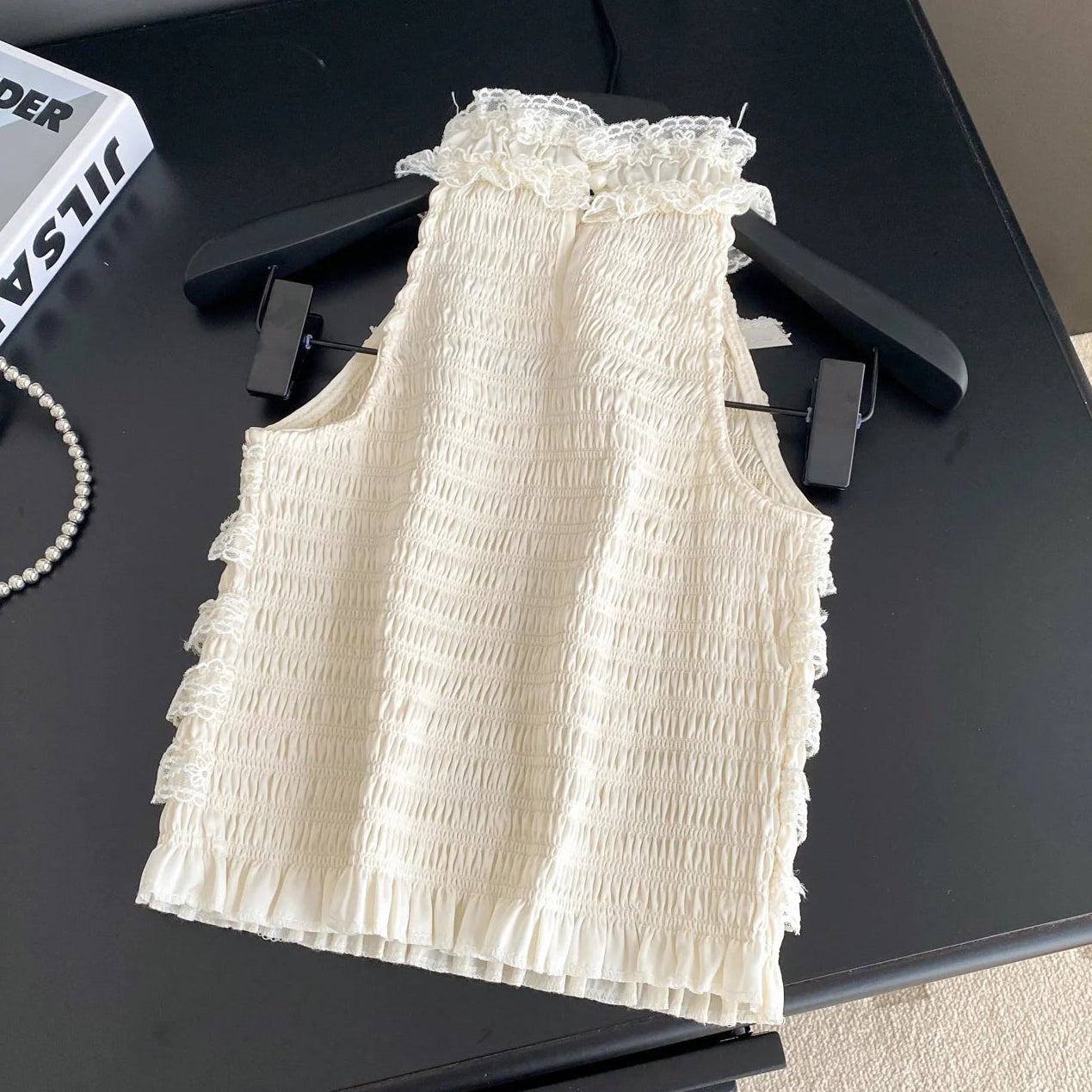 White ruffled top on a black surface with a book and jewelry nearby