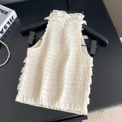White ruffled top on a black surface with a book and jewelry nearby