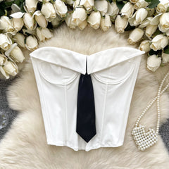 White strapless top with a black tie on a fur surface surrounded by white roses and pearls.