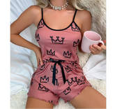Woman wearing a pink pajama set with black crowns, holding a pink mug.