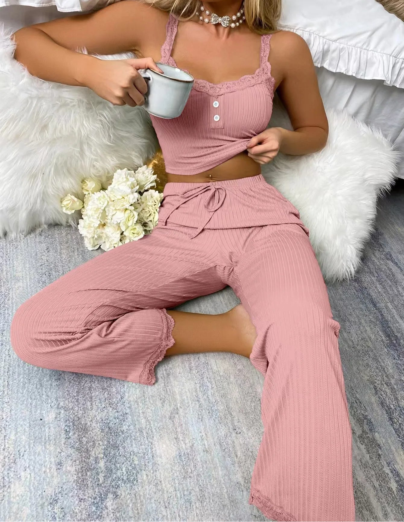 Woman in pink ribbed top and pants holding a mug, sitting on a fluffy white chair with flowers beside her.