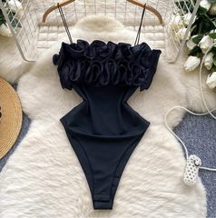 Black swimsuit with ruffled top on a white fur rug surrounded by decorative items.