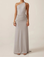 Woman wearing a long, light gray one-shoulder dress against a plain background