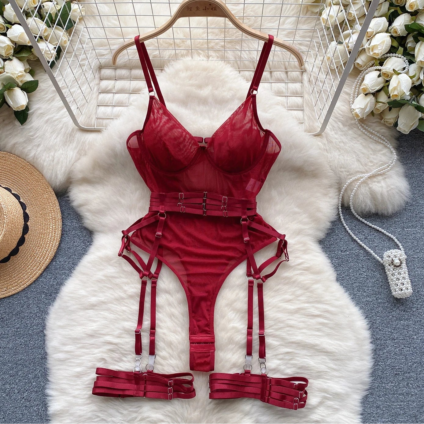 Red lingerie set on a hanger with flowers and a hat in the background