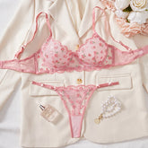 Pink lingerie set with a blouse, floral arrangement, and perfume bottle on a white background