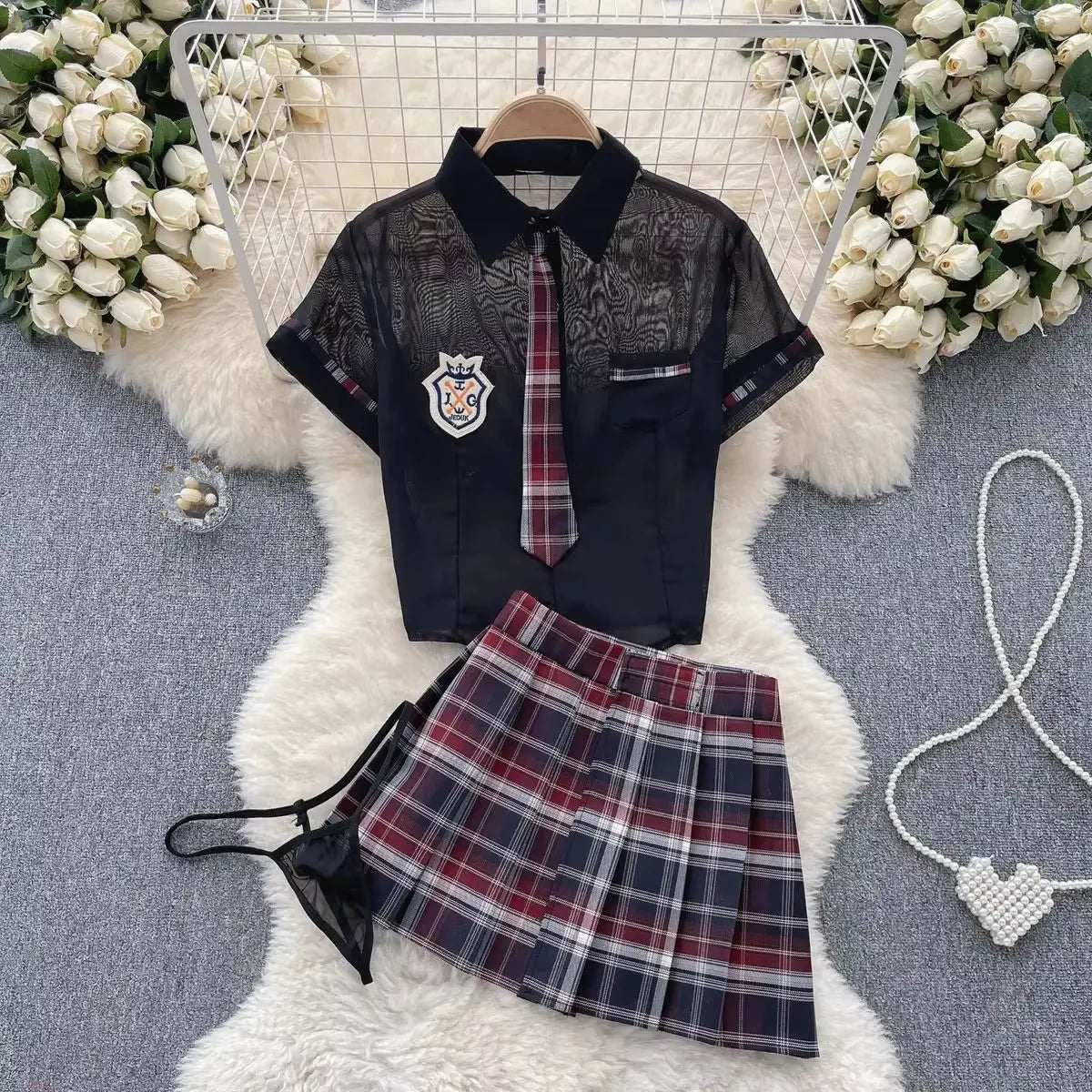 School uniform with black shirt, plaid skirt, and tie on a white fur rug with floral decorations.