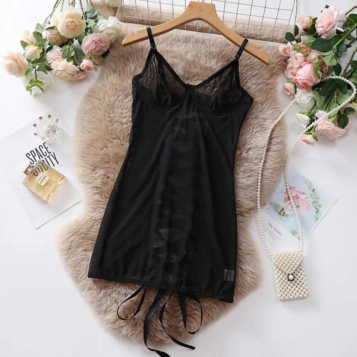 Black slip dress on a hanger with flowers and a bag on a textured surface