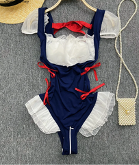 Navy blue swimsuit with white ruffles and red accents on a gray surface.