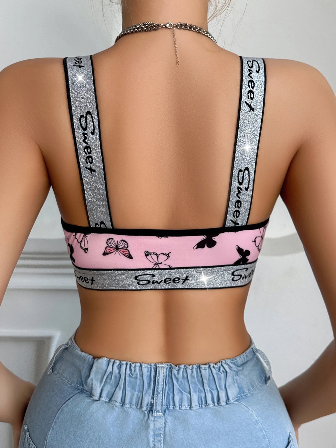 Person wearing a sports bra with 'Sweet' branding and pink butterfly design, paired with light blue jeans.