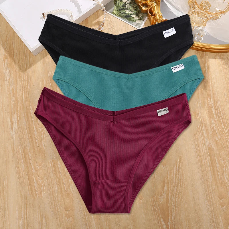 Three pairs of ribbed underwear in black, teal, and burgundy on a wooden surface.