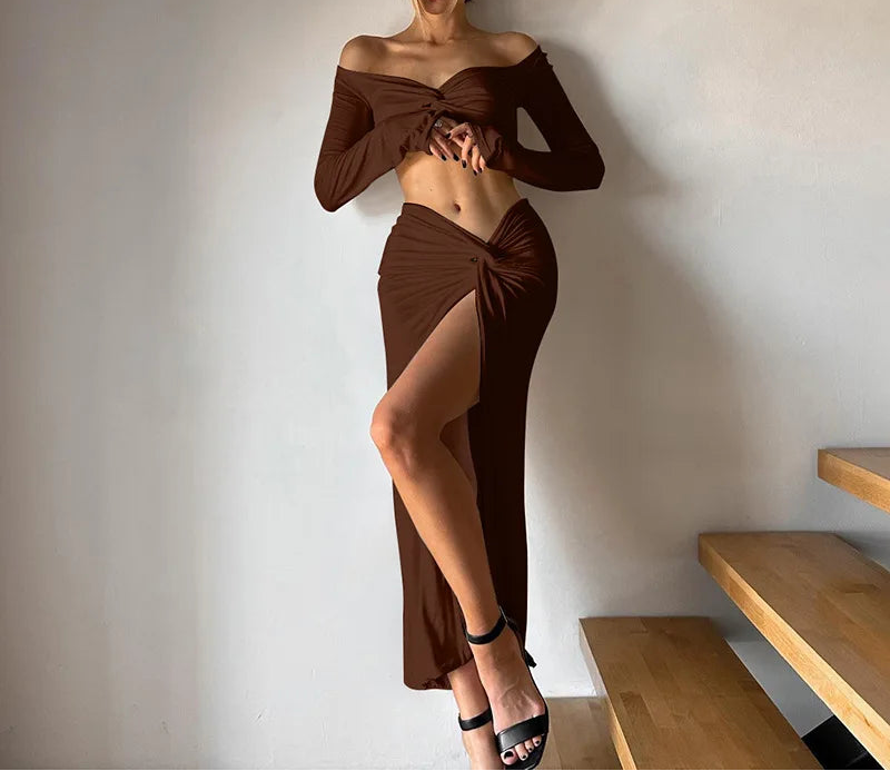 Woman in a brown off-shoulder top and skirt standing against a plain wall.