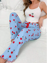 Woman wearing a white tank top and blue pants with red cherry pattern on a white couch.