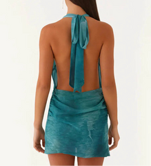 Woman wearing a teal halter dress with a tie detail on a white background