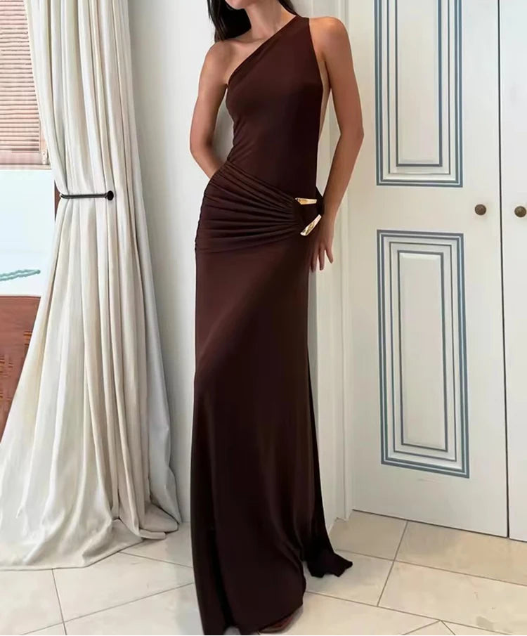 Woman wearing a brown one-shoulder dress standing in a room with white curtains and a white door.