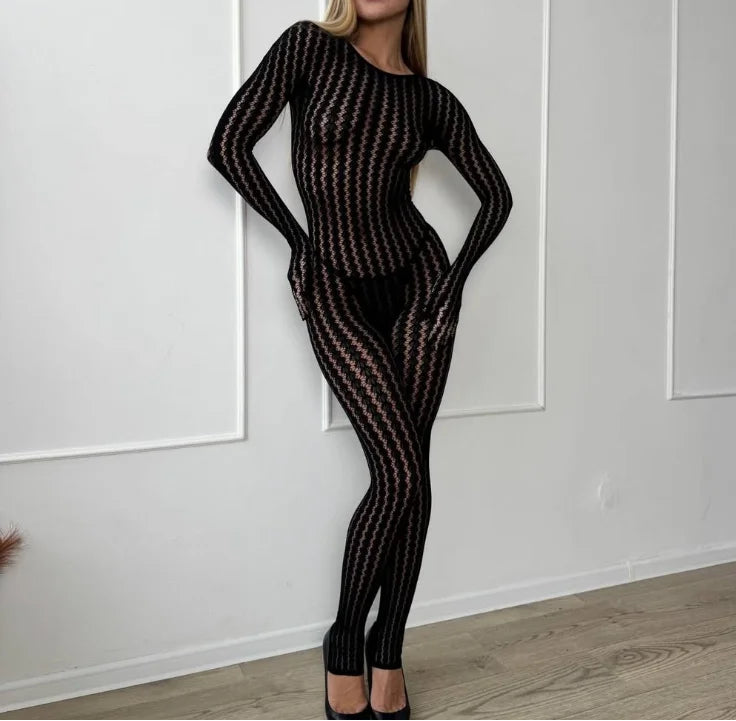 Woman wearing a black fishnet outfit against a white paneled wall.