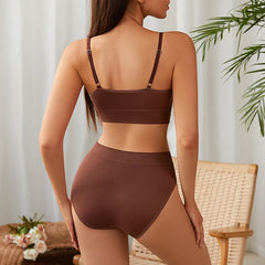 Woman wearing a brown bikini set in a home setting with a plant and chair.