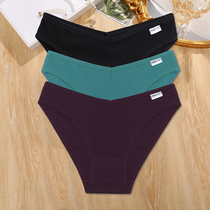 Three pairs of women's underwear in black, teal, and purple on a wooden surface.