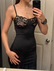 Person wearing a black dress with lace details, taking a mirror selfie.