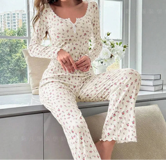 Woman wearing a floral pajama set sitting by a window with books and flowers.