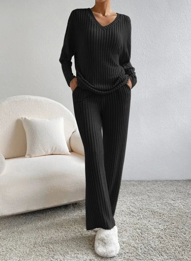 Person wearing a black ribbed sweater and pants in a minimalistic room with a white sofa.