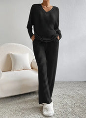 Person wearing a black ribbed sweater and pants in a minimalistic room with a white sofa.