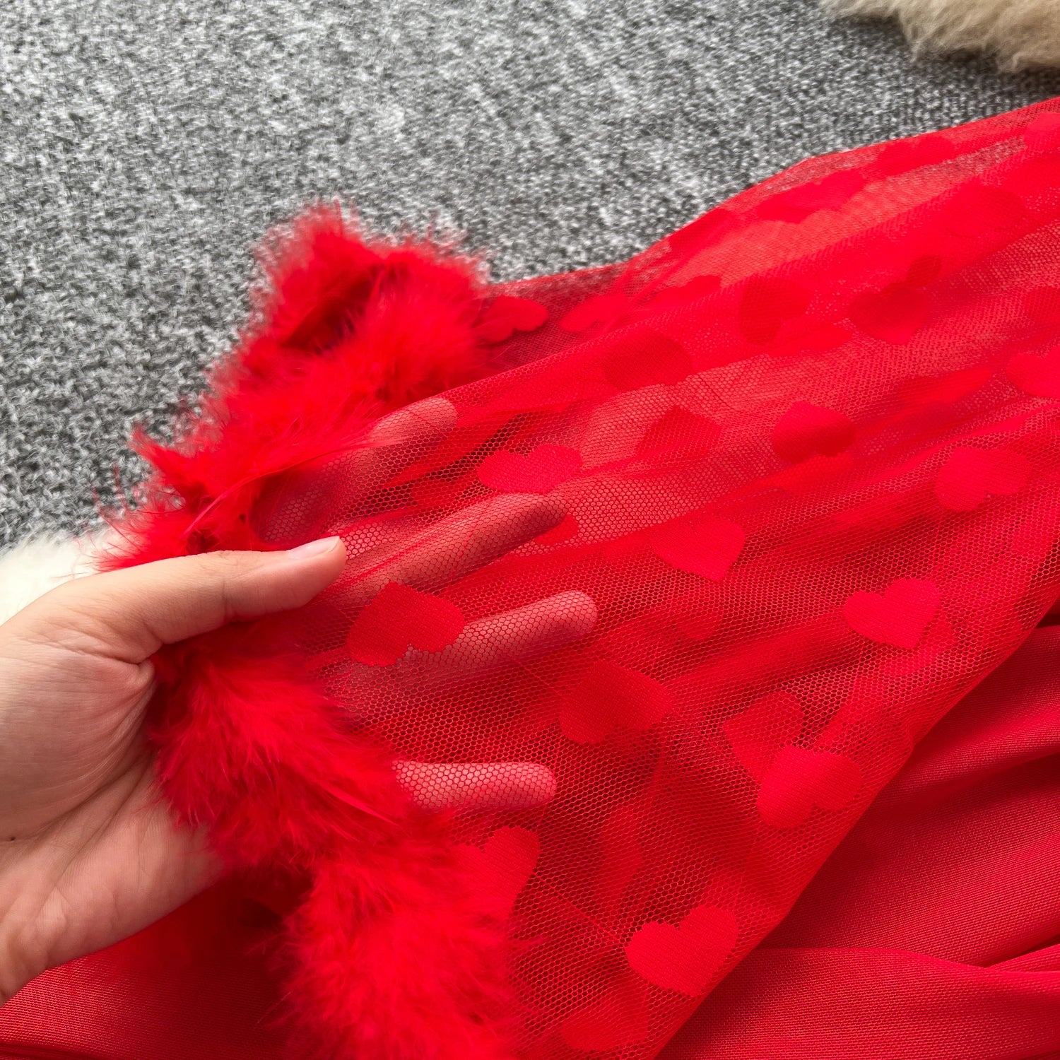 Red fabric with heart patterns held by a hand on a textured surface