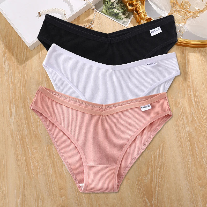Three pairs of underwear in black, white, and pink on a wooden surface.