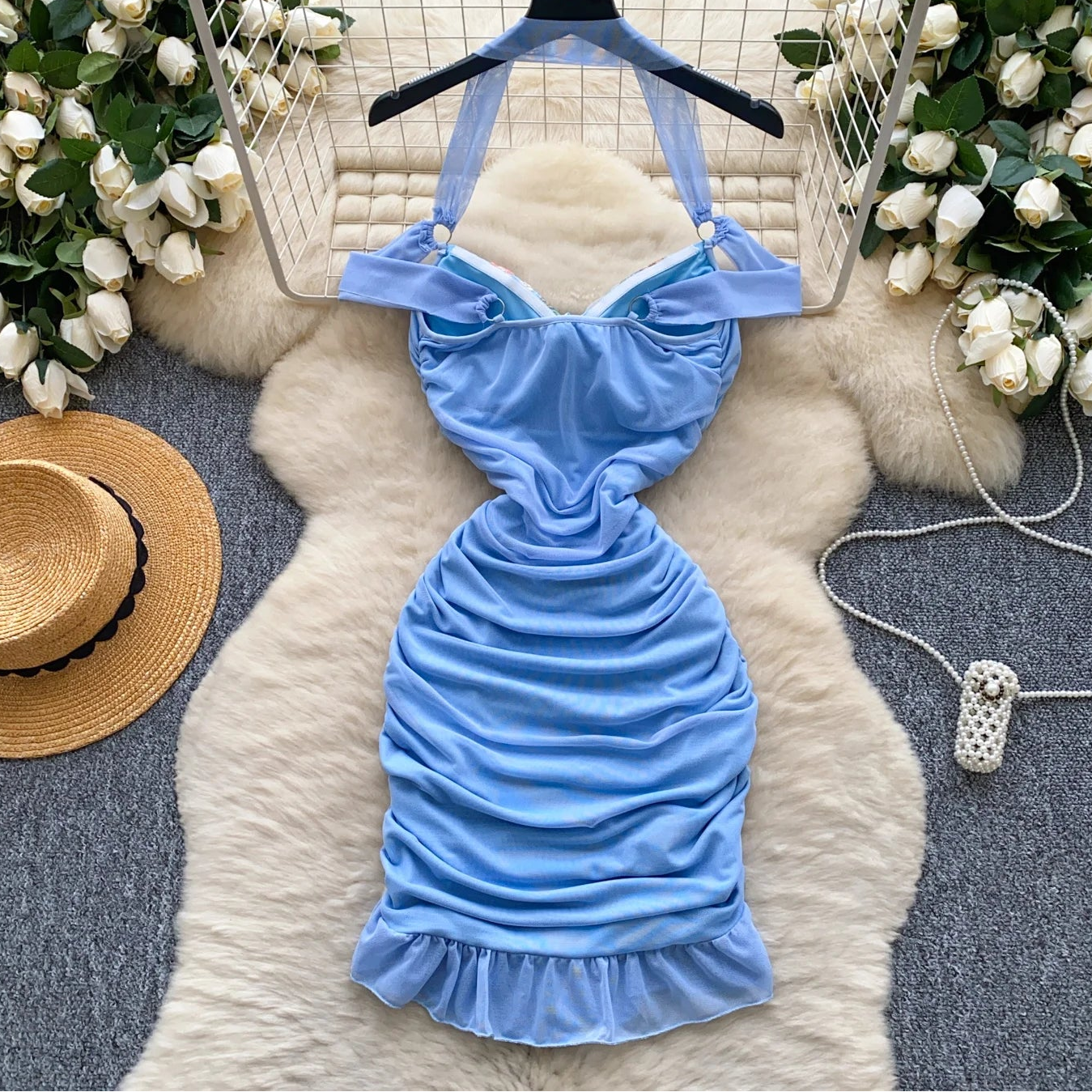 Blue halter dress on a hanger with decorative flowers and a hat in the background