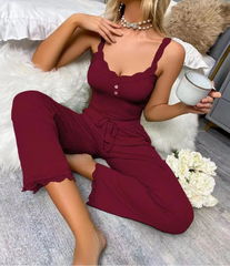 Woman in burgundy jumpsuit sitting on a bed holding a mug.