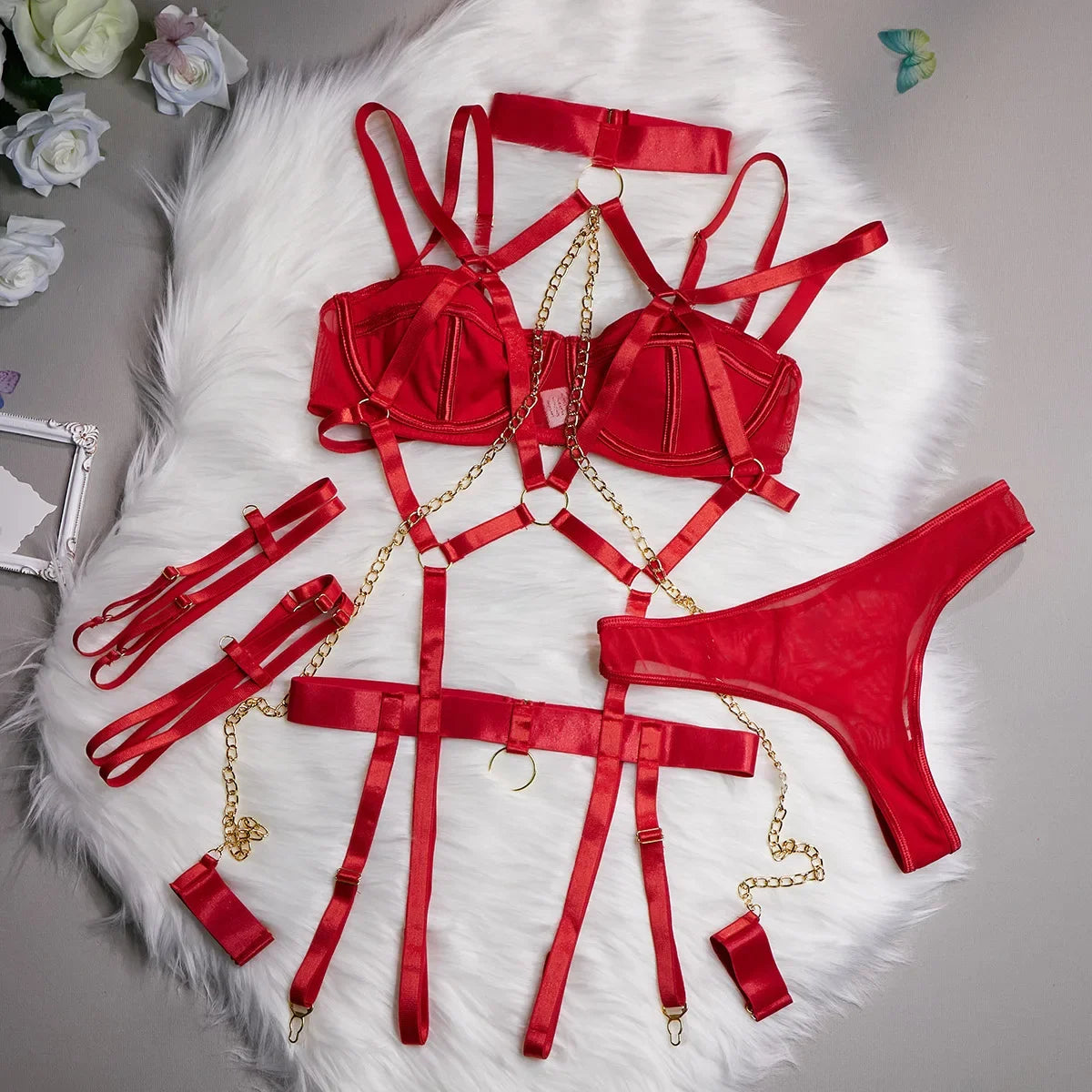 Red satin lingerie set with gold chains on a white fur surface.