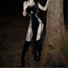 Woman in a black outfit with tattoos standing next to a tree in a dark forest