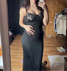 Woman taking a mirror selfie wearing a black lace dress in a room with wooden walls.