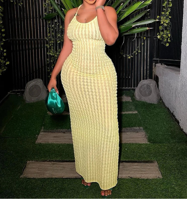 Woman in a yellow dress holding a green clutch against a dark background with plants.