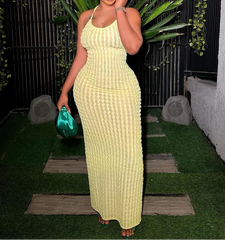 Woman in a yellow dress holding a green clutch against a dark background with plants.