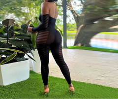 Woman in a black outfit standing outdoors with greenery in the background