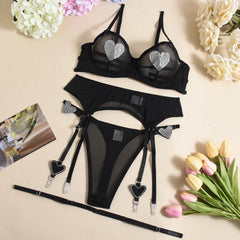 Black lingerie set with heart details on a beige surface with flowers and a magazine.