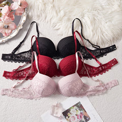Set of black, red, and pink lace bras on a textured surface with flowers and a mirror.