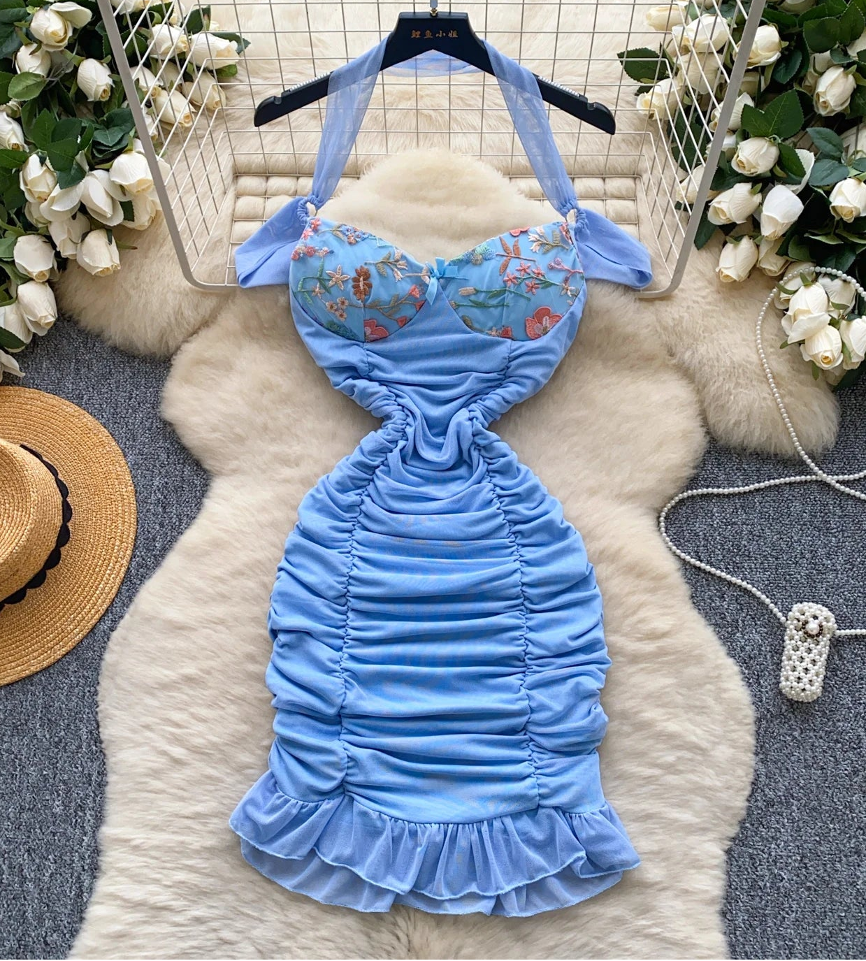 Blue mermaid-style dress with floral top on a fur rug surrounded by flowers and a hat.