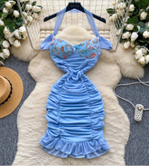 Blue mermaid-style dress with floral top on a fur rug surrounded by flowers and a hat.
