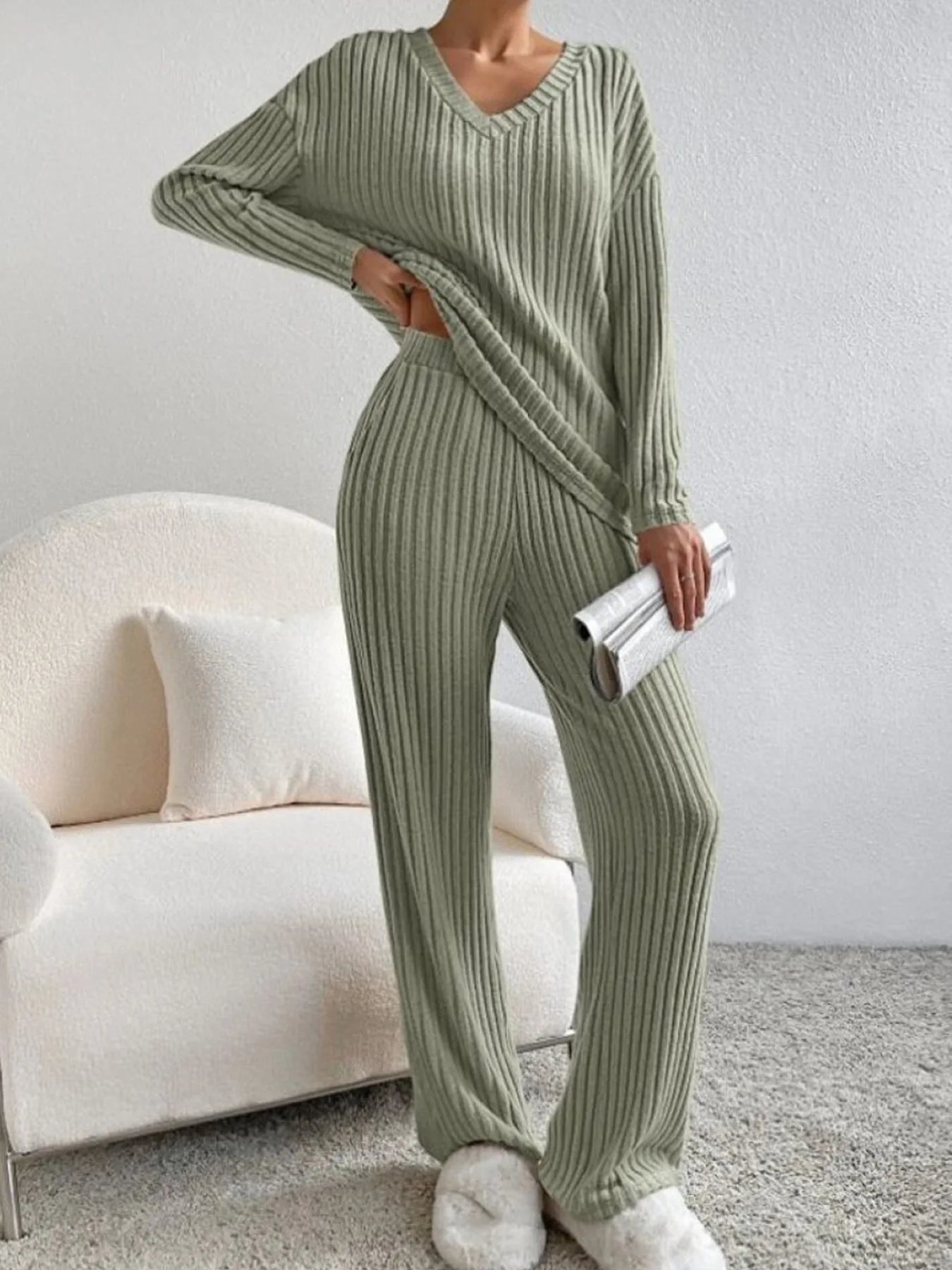 Person wearing a green ribbed sweater and pants set in a living room.