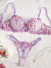 Floral lingerie set with purple straps on a textured white surface.