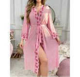 Pink robe with floral lace details worn by a model in a bedroom setting