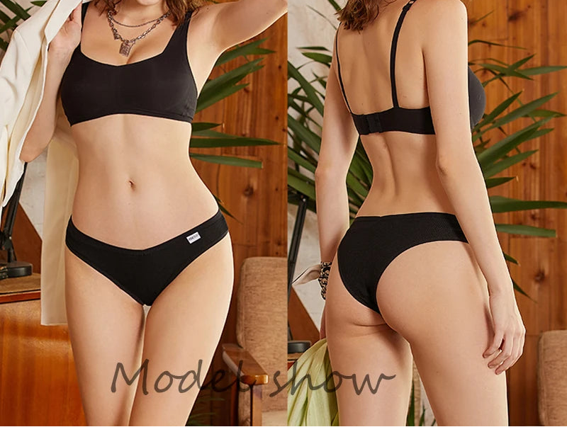 Woman modeling black lingerie set in a home setting with plants and wooden furniture.