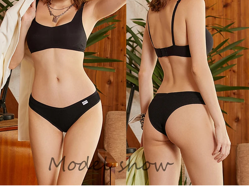Woman modeling black lingerie set in a home setting with plants and wooden furniture.