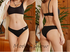 Woman modeling black lingerie set in a home setting with plants and wooden furniture.