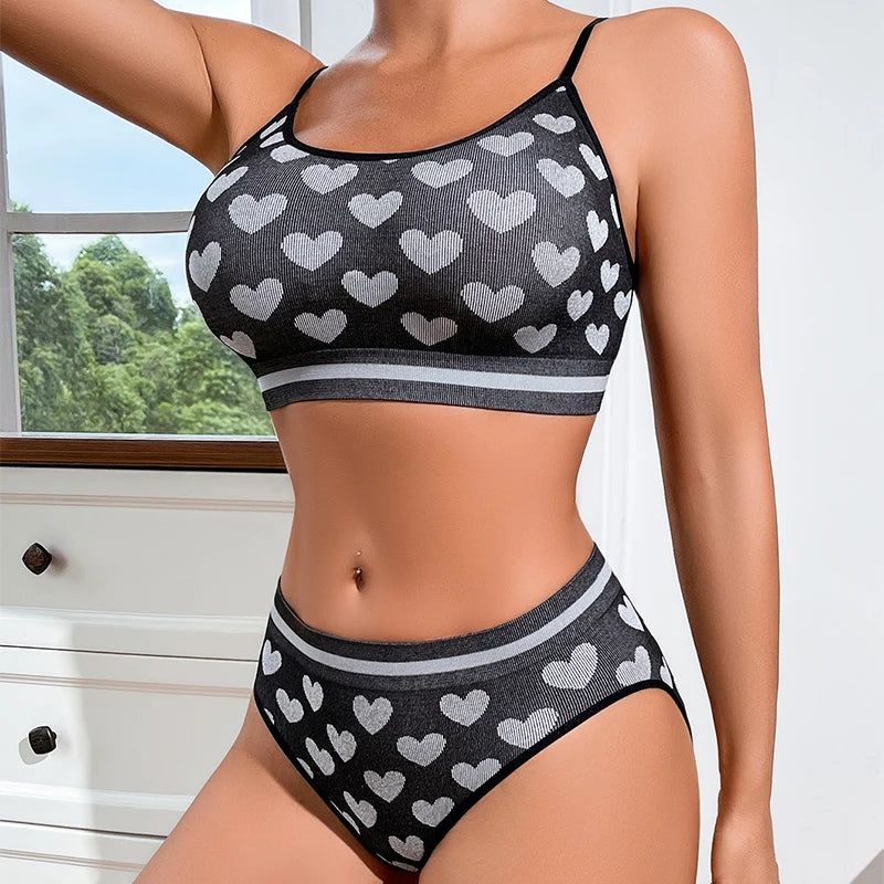 Woman wearing a black and gray heart-patterned bikini set with a window and greenery in the background.