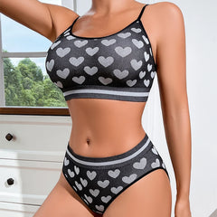 Woman wearing a black and gray heart-patterned bikini set with a window and greenery in the background.