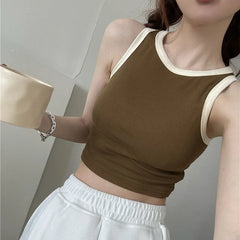 Person wearing a brown tank top with white trim and white pants in a neutral setting
